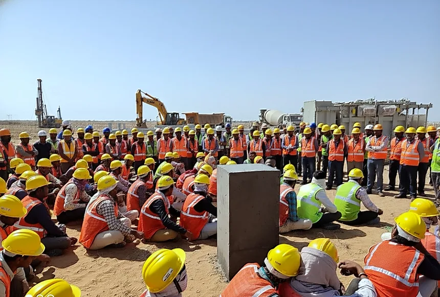 Morning safety briefing before the shift, with piling rig and excavator on standby